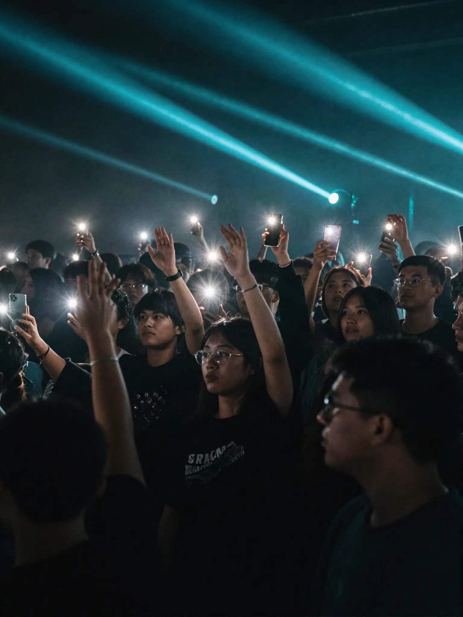 Fans with raised hands and phone lights at a live show